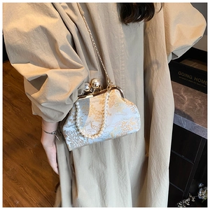 Detailed view of elegant jacquard handbag with pearl clasp and chain on beige trench coat