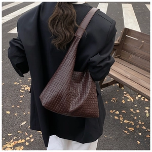 Detail of a large dark brown woven hobo bag with wide shoulder strap on a model