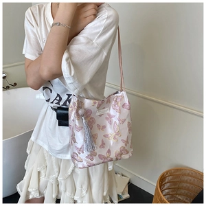 Detail of light pink shoulder bag featuring butterfly embroidery and tassel charm