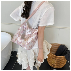 Sac seau en satin rose avec broderie papillon dorée et pompon porté à l'épaule