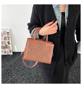 Detail of vintage brown embossed tote bag with floral patterns and gold hardware on model