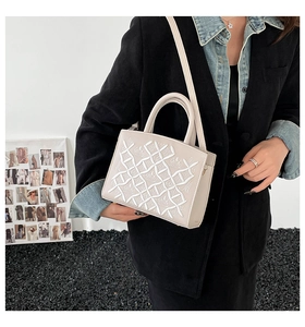 Detailed close-up of cream faux leather handbag with white geometric embroidery and hardware