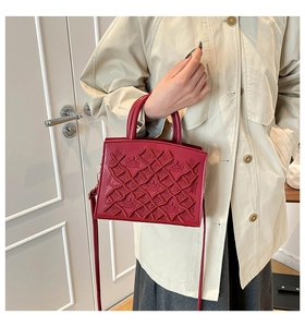 Close-up of wine red embossed handbag with crown pattern worn with a beige trench coat