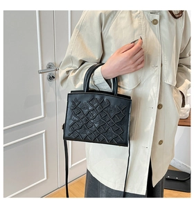 Detail of black patent leather bag with embossed weave pattern on a beige trench coat