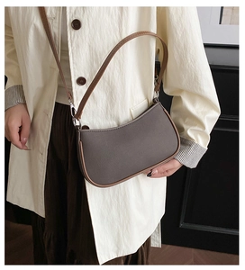 Close-up of grey textured crescent bag with brown leather strap worn by a model