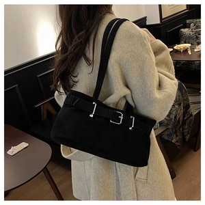 Detail of a black matte shoulder bag with metallic buckle straps on a beige coat