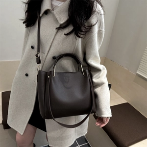Borsa a secchiello marrone scuro con trama litchi e tracolla indossata con cappotto beige