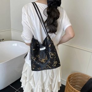 Grand sac cabas noir avec imprimé papillon doré porté par un mannequin dans un salon