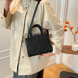 Classic black lady handbag with geometric embossed texture shown on model side view