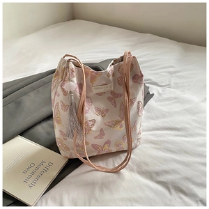 Gros plan sur la broderie papillon et le pompon gris d'un sac cabas en toile beige