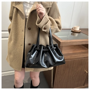 Detailed shot of black patent leather shoulder bag with chic ruched texture on a model