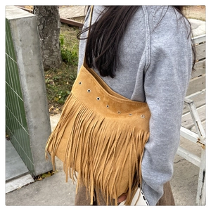 Sac bandoulière en daim marron avec franges longues et œillets métalliques en vue lifestyle extérieur