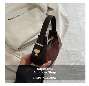 Detail of adjustable shoulder strap and gold zipper on brown crescent handbag
