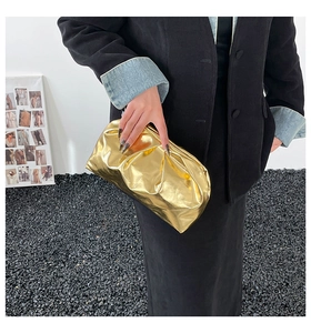Detail of golden pleated cloud clutch bag with metallic texture and mirror effect finish