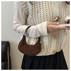 Close-up of brown suede half-moon bag with gold hardware worn by a model in winter outfit
