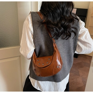 Model view of a vintage brown half-moon bag with metallic studs and wide leather strap