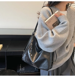Detail of a soft black leather tote bag with side zipper and tassel accents worn on shoulder