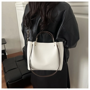 White pebbled leather tote bag with brown handles styled on a model's shoulder