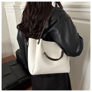Detail of off-white tote bag showing pebbled leather texture and gold metal bar handle
