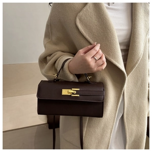 Détail du sac à main en cuir marron foncé avec fermoir doré sur un manteau en laine