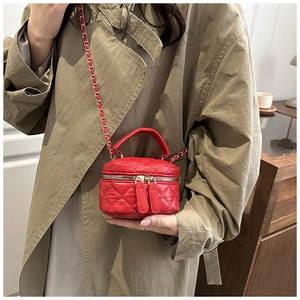 Detail of a red quilted mini crossbody bag with chain strap worn by a model in a trench coat