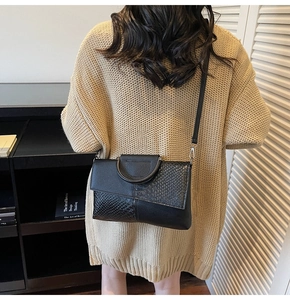 Detail of model wearing black snakeskin embossed shoulder bag with unique metal handle
