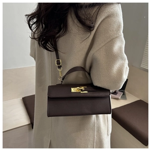 Détail d'un mini sac bandoulière marron foncé avec fermoir doré porté sur manteau beige