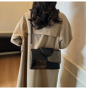 Detail of trendy crossbody bag featuring black grained leather and snakeskin pattern