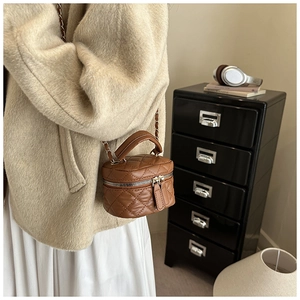 Detailed side view of a brown quilted mini bucket bag with gold chain and top handle