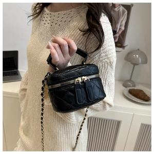 Close-up of black quilted mini box bag with gold chain strap on an indoor cream background