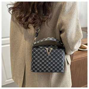 Detail of grey patterned crossbody bag with gold V clasp on grey wool coat