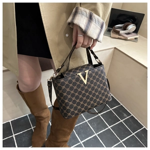 Detail of a brown plaid patterned handbag featuring a gold V-shaped buckle and luxury strap