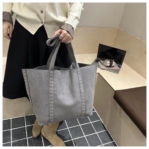 Detail showing silver rivet studs on grey suede tote bag held by model in lifestyle setting