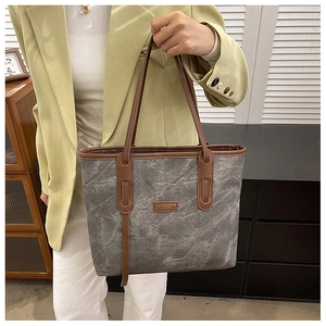 Chic grey tote bag with brown leather trim carried by a model in a stylish blazer