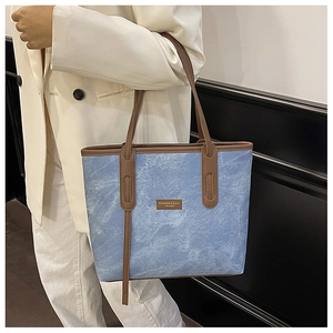 Close-up of blue denim tote bag with brown leather handles and golden logo detail