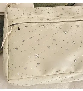 Détail du sac à bandoulière en toile beige avec broderies d'étoiles argentées et texture
