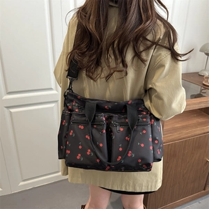 Fashionable black cherry print crossbody bag with multiple zippers shown on a model