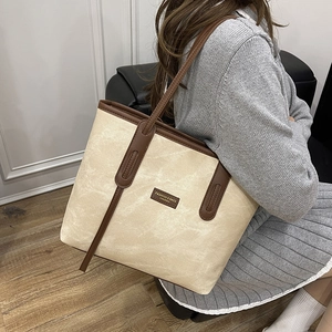 Chic beige marble patterned tote bag with brown handles, shown worn by a model