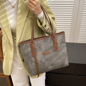 Chic grey canvas tote bag with brown leather handles worn by model in sunny setting