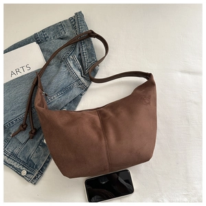 Flat lay of brown suede crescent bag with adjustable strap and casual accessories