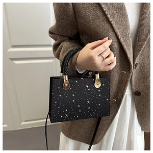 Detail of black crossbody bag with white star pattern worn with a brown blazer and white skirt