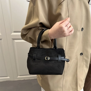 Sac à main noir mat grande capacité avec boucle dorée présenté avec un trench-coat