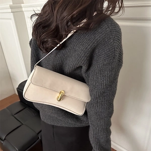 Borsa a spalla minimalista in pelle beige con chiusura dorata indossata su maglione