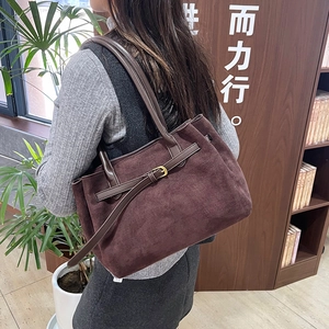 Large brown suede tote bag with decorative gold buckle shown in a lifestyle setting