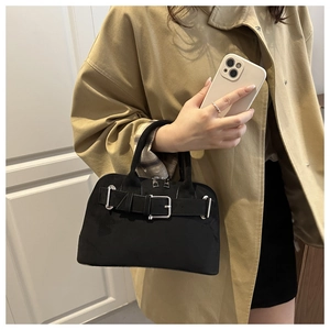 Close-up of black matte shell bag featuring silver metal buckle and double handles