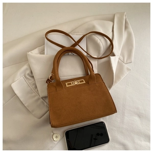 Brown suede crossbody bag with gold buckle detail on a chic beige blazer background