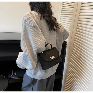 Sac à bandoulière matelassé noir avec fermoir doré porté par un mannequin en pull gris clair