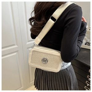 Détail du sac photo tissé beige avec logo M doré et large bandoulière sur modèle