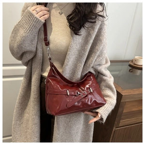 Detail of dark red glossy underarm bag with pleated design and silver eyelet strap