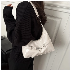 Model wearing a stylish cream off-white patent leather half-moon shoulder bag with silver buckle